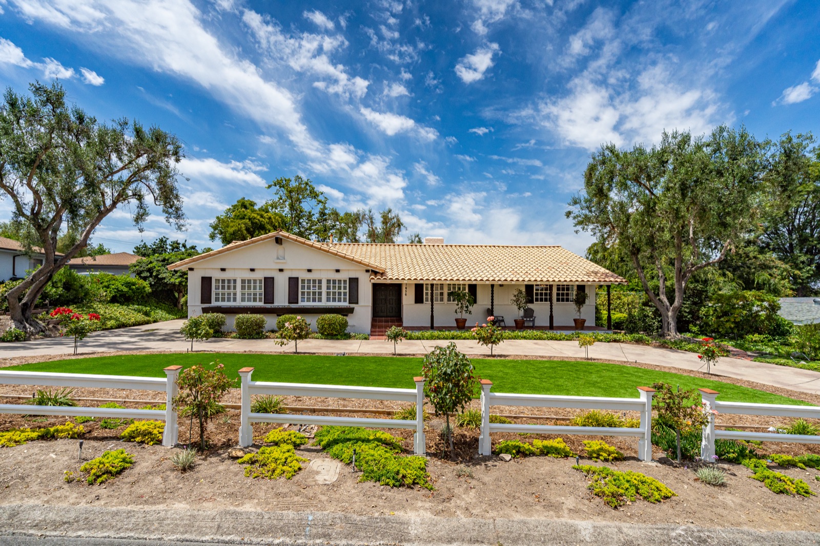 Daytime photo of a single-story ranch home with a white fence, before editing